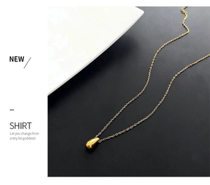 Close-up of a polished gold teardrop pendant on a fine link chain over a dark background