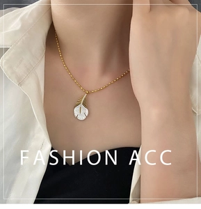 Détail du collier à billes dorées avec pendentif plume en nacre et serti de zircons brillants