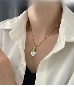 Détail d'un collier chaîne à billes dorées avec pendentif plume en nacre élégante