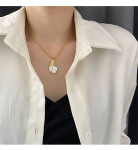 Gros plan du pendentif plume en or avec nacre sur une femme portant une chemise