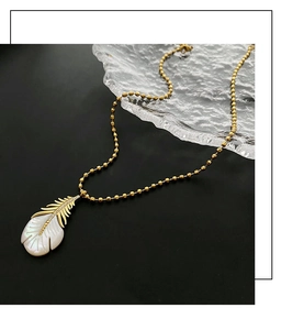 Détail d'un pendentif plume doré avec nacre blanche et détails en zircon sur chaîne à billes