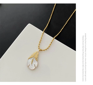 Détail du pendentif plume dorée avec nacre et zircons sur une chaîne à billes dorée