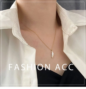 Détail d'un collier pendentif triangle doré avec incrustation blanche sur une chemise blanche
