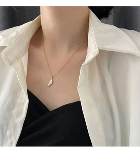 Gros plan d'un collier en titane doré avec un pendentif triangle blanc porté par un mannequin