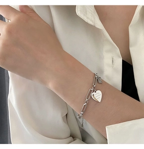 Dettaglio del bracciale a catena con ciondolo a cuore inciso e targhetta rettangolare