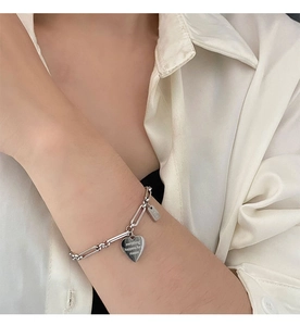 Vista macro del bracciale in argento con ciondolo a cuore inciso su fondo di raso