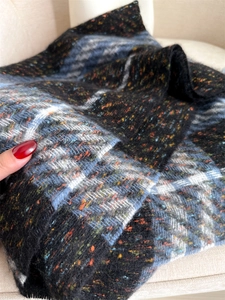 Close-up of soft multi-color plaid scarf featuring classic fringe and thick knit texture