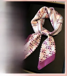 Close-up of elegant silk scarf with gold chain print and burgundy borders in a black tray