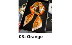 Detailed view of an orange silk-like scarf with equestrian chain prints in a tray