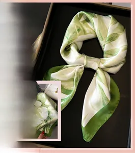 Detail of silk-like scarf featuring green floral prints and dark green hemmed edges