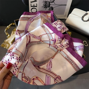 Detailed texture of ivory silk scarf with purple chain patterns and gold buckle accents