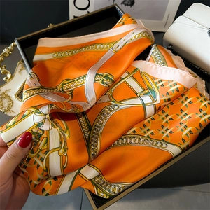 Detailed macro of vibrant orange satin square scarf featuring golden chain and equestrian motifs