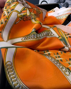 Close-up of orange silk scarf showing satin texture and classic chain print pattern