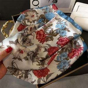 Detail of silk-like scarf with floral prints and blue rolled edges on a metal tray