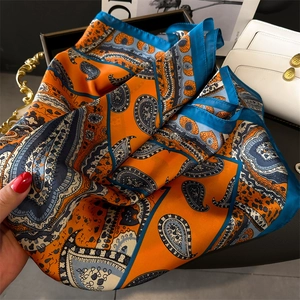 Detail of silk-like scarf with orange and blue paisley print near a luxury handbag