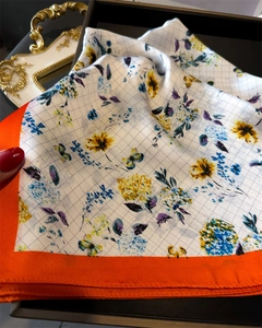 Detailed view of floral silk scarf with yellow flowers and orange contrast borders