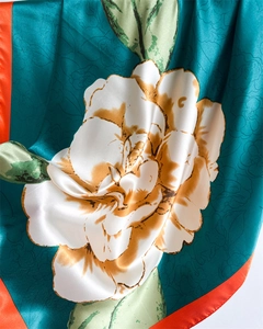 Close-up of satin scarf with camellia print in peacock blue and orange silk fabric