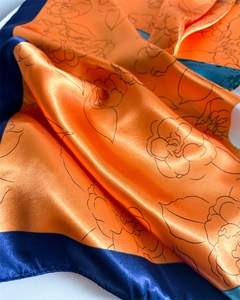 Detailed macro view of the silky orange and navy floral satin scarf showing texture