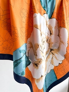 Close-up of orange satin scarf with large white camellia print and floral texture