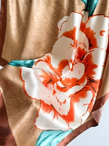 Detail of satin silk scarf featuring large orange floral prints and champagne gold base