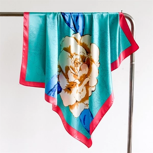 Detail of teal satin scarf with floral prints and red rolled hem on metal hanger