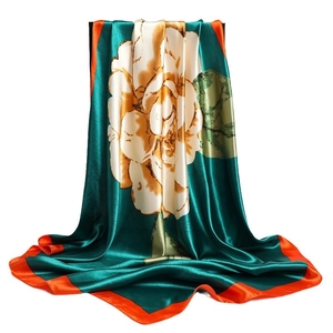 Deep green satin scarf with floral print and vibrant orange borders draped on a stand