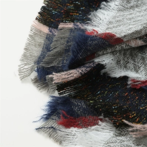 Gros plan sur le motif en tricot coloré et franges du châle poncho à carreaux et capuche