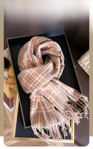 Detail of winter checkered scarf with long tassels in orange and beige cashmere-like fabric