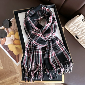 Detailed view of red, black and white plaid scarf with tassels on stylish backdrop