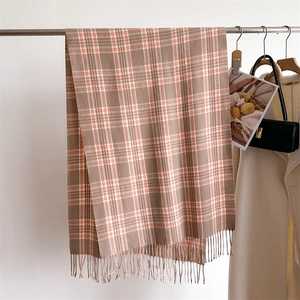Detailed view of checkered scarf with tassels hanging next to an elegant white coat