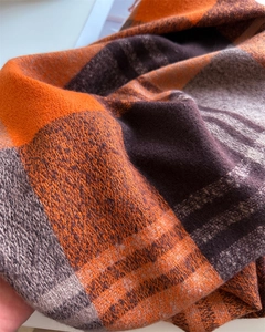 Close-up of soft rainbow plaid scarf texture with orange and brown knitted fringe detail