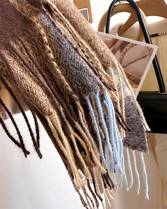 Close-up of thick knit winter scarf with long tassels and brown beige blue plaid pattern
