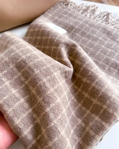 Détail de la texture douce d'une écharpe à carreaux tons terre avec franges et tissage