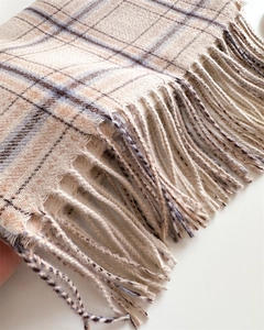 Gros plan sur la texture en cachemire à carreaux beige et bleu et les franges du foulard