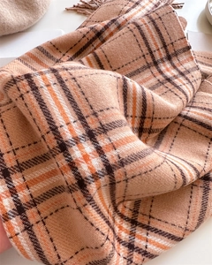Gros plan sur une écharpe épaisse à carreaux orange et beige avec des franges douces