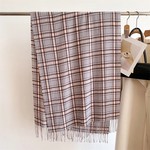 Détail d'une écharpe à carreaux gris et rose avec franges suspendue dans un vestiaire