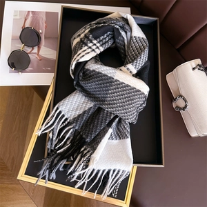 Dettaglio macro di sciarpa a quadri simil-cashmere con frange su vassoio nero elegante
