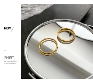 Detailed close-up of two gold titanium steel rings with zircon stones on a mirror surface