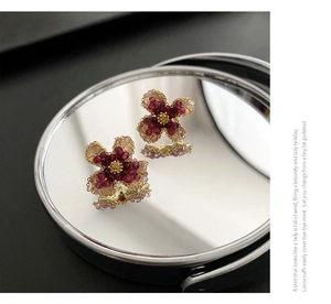 Detailed view of handcrafted flower earrings with red beads on a mirror surface