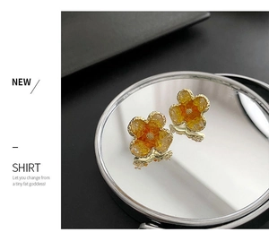 Macro shot of sweet orange floral stud earrings on a reflective mirror surface