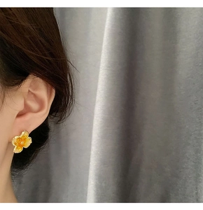 Macro close-up of orange floral enamel stud earring worn by model on grey background
