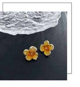 Macro detail of orange four-leaf clover earrings with gold metal edges and stone texture