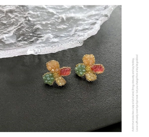 Macro detail of colorful four-petal floral stud earrings with faceted beads on dark stone