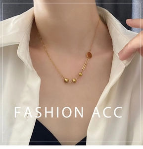 Detail view of asymmetric gold necklace featuring polished metal beads and a rectangular link