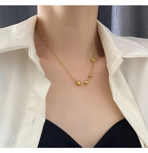 Detailed view of asymmetric gold ball pendant and twisted chain necklace on collarbone