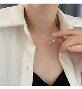 Close-up of a minimalist gold-plated necklace with three small beads on a model