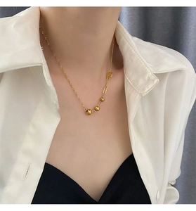 Detail of asymmetric gold bead necklace showing polished spheres and rectangular chain link