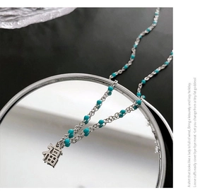 Détail du collier avec pendentif Fu argenté et perles bleu clair sur un miroir rond