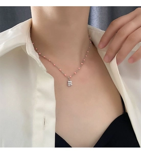 Gros plan d'un collier en argent avec perles roses et pendentif carré caractère Fu