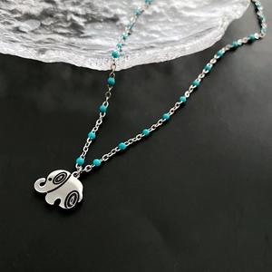 Minimalist silver elephant pendant necklace with turquoise bead chain on black background
